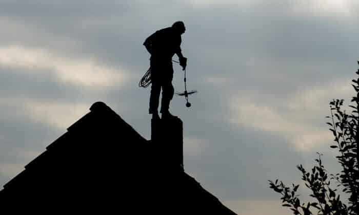 A chimney sweep stands above a chimney